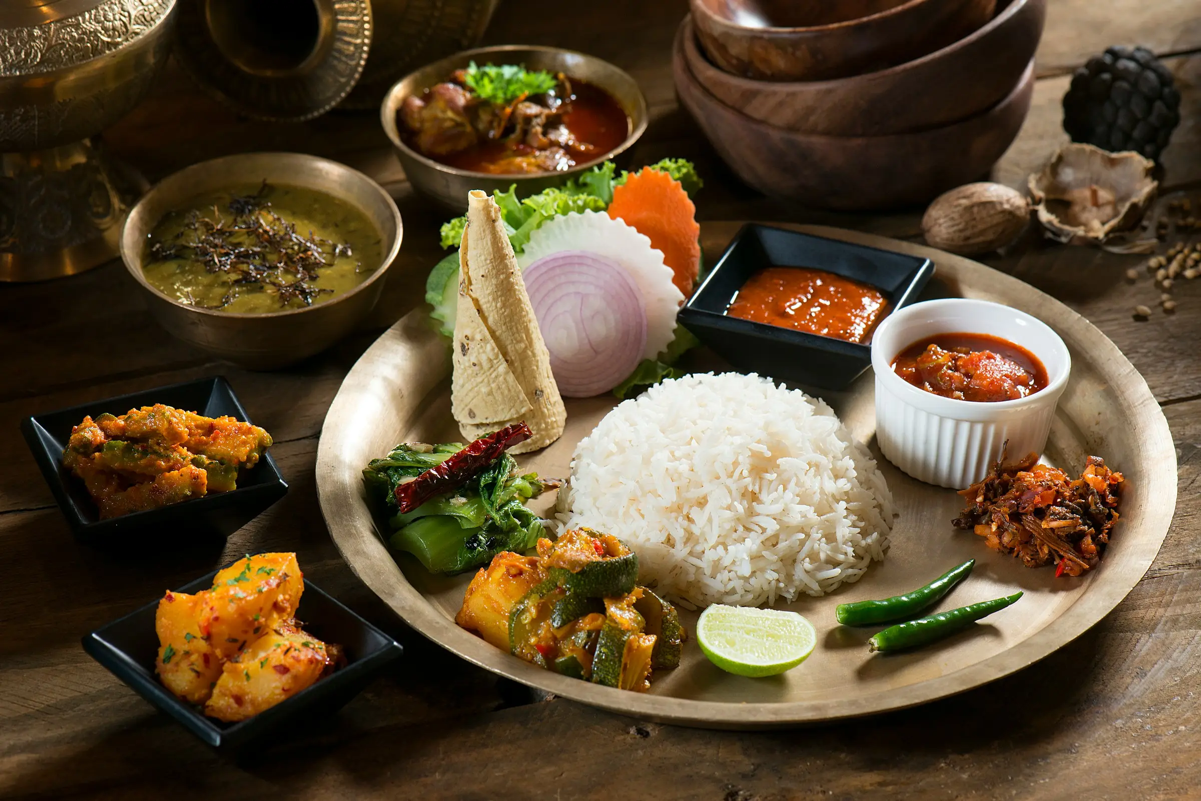 Traditional Nepali dal bhat thali on a brass plate with rice, lentil soup, curries, pickles and papad on a dark wooden table